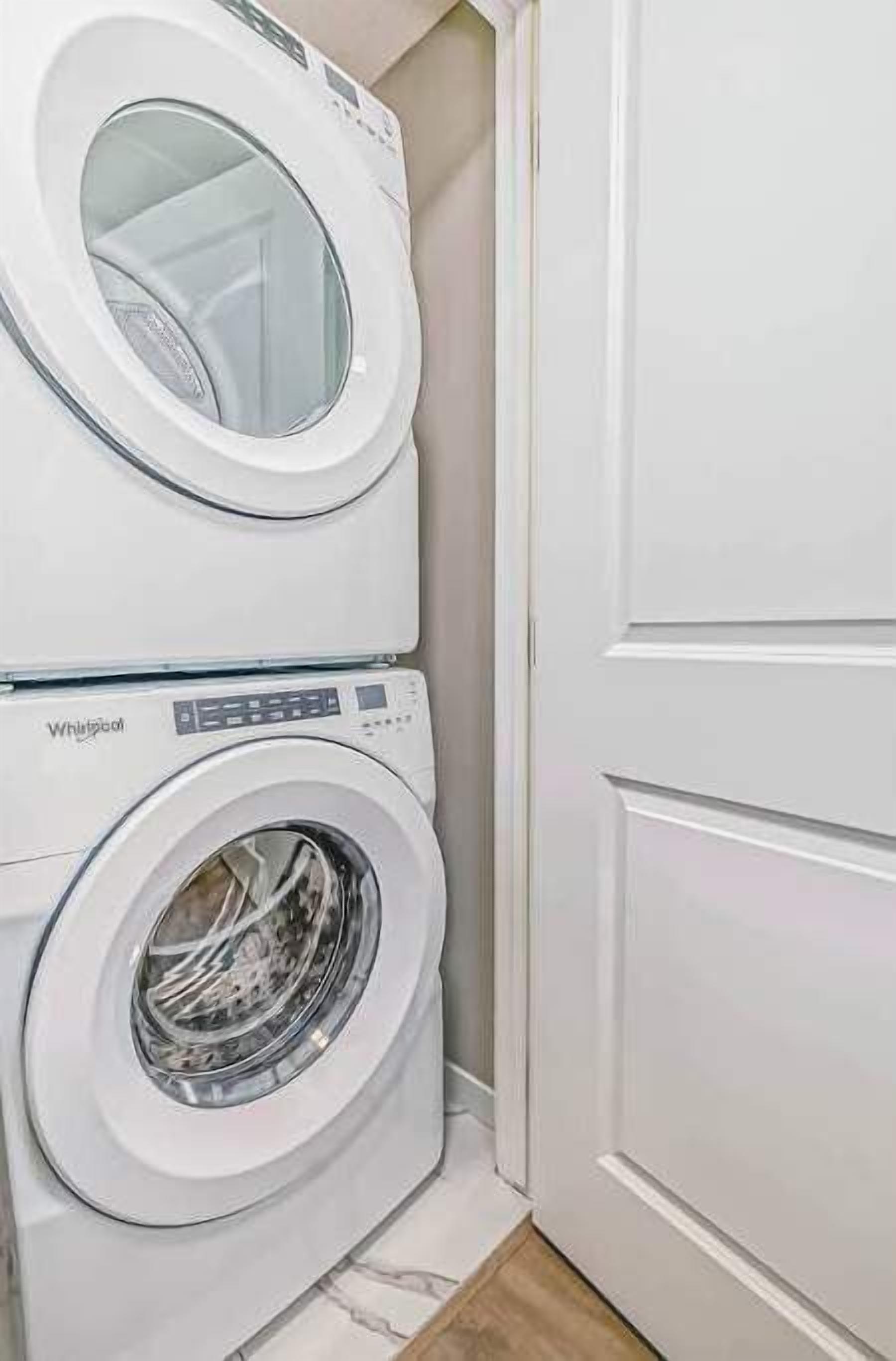 A stacked washer and dryer unit in a room with a white door and tiled floor.