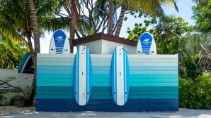 A pool area with two surfboards mounted on a wall, surrounded by palm trees and a clear blue pool. - 7 Mile Beach Penthouse Style Condo with Pool View and Rooftop (West Bay)