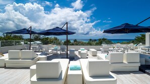 A rooftop lounge area with white cushioned seating and umbrellas, overlooking a scenic ocean view. - 7 Mile Beach Penthouse Style Condo with Pool View and Rooftop (West Bay)