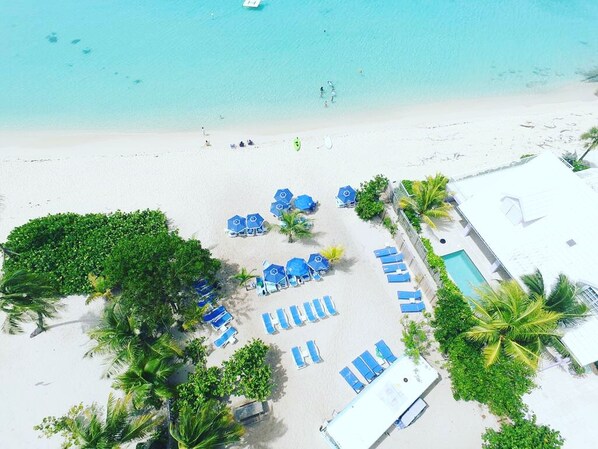 An aerial view of a beach resort with sun loungers, a pool, and palm trees.
