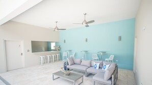 A spacious living area with a light blue wall, a gray sofa set, a coffee table, and two ceiling fans. - 7 Mile Beach Penthouse Style Condo with Pool View and Rooftop (West Bay)