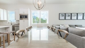 A modern kitchen with white cabinets, a stainless steel microwave, and a dining area with a glass table and wooden chairs. - 7 Mile Beach Penthouse Style Condo with Pool View and Rooftop (West Bay)