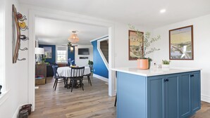 Een moderne keuken met blauwe kastjes, een wit aanrecht en een eethoek met een tafel en stoelen.