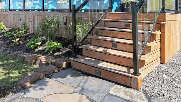Een huis met een houten terras, buitenmeubels en een stenen pad naar de ingang.