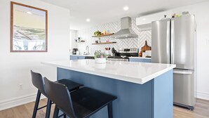 Een moderne keuken met een centraal eiland, barkrukken, een roestvrijstalen koelkast en een backsplash met een visgraatmotief.