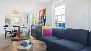 Een moderne woonkamer met een blauwe bank, een houten salontafel en een eethoek met een witte tafel en stoelen.