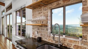 Une cuisine avec un mur en pierre, de grandes fenêtres et une vue sur la campagne.