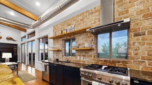 Une cuisine moderne avec un mur en briques, des appareils électroménagers en acier inoxydable et une grande fenêtre donnant sur un paysage pittoresque.