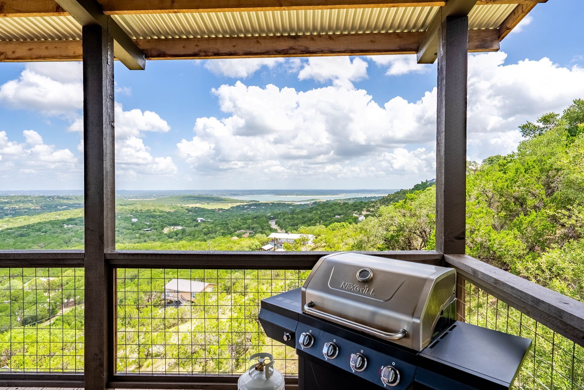 Een overdekt buitengebied met een barbecue en uitzicht op een groen landschap.