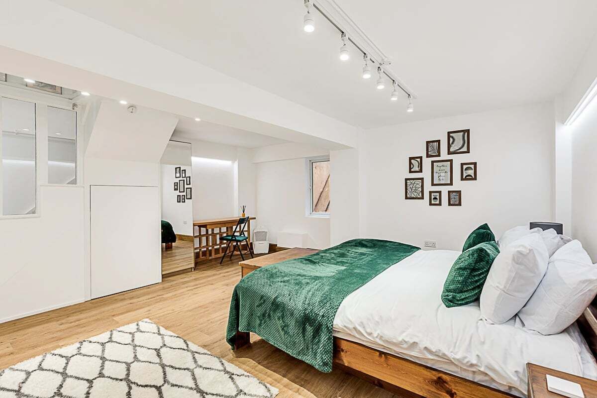 A modern bedroom with a wooden bed, a green throw blanket, and a white rug.