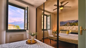 Ein Hotelzimmer mit einem Bett, einem Nachttisch mit einer Vase und einer Kaffeetasse-Unterlage, einem Fenster mit Blick auf Berge und einem Deckenventilator.