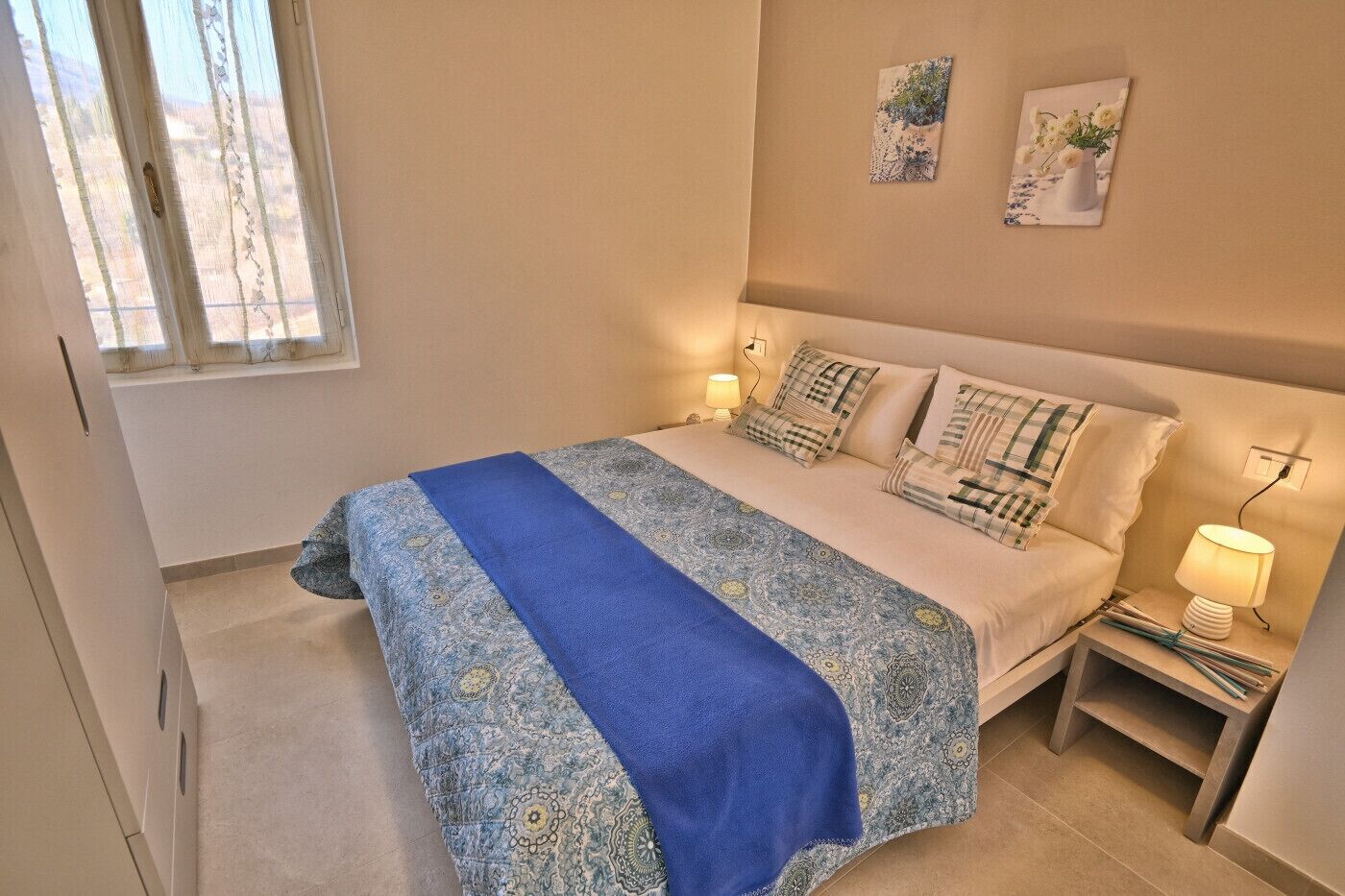 A bedroom with a bed, two bedside tables, a window, and wall art.