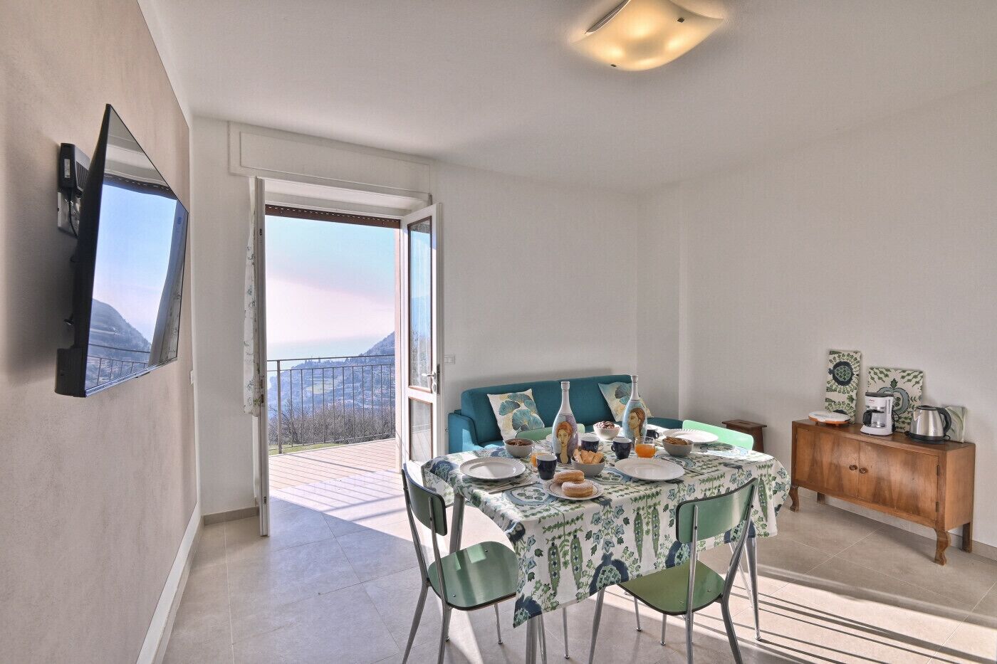 A dining area with a table set for breakfast, a sofa, and a view of the outdoors.