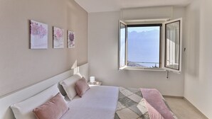 Un dormitorio con cama, mesita de noche, ventana con vista a las montañas y tres cuadros colgados en la pared.