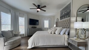 Une chambre spacieuse avec un grand lit, un ventilateur de plafond, une télévision et une commode moderne.