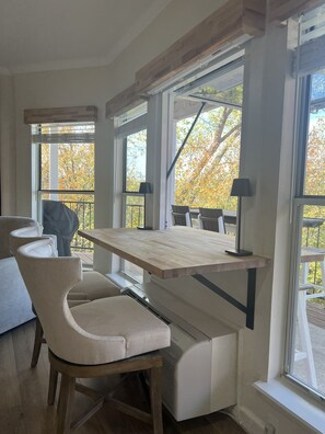 A modern kitchen with a wooden table, a built-in bench, and large windows offering a view of trees.