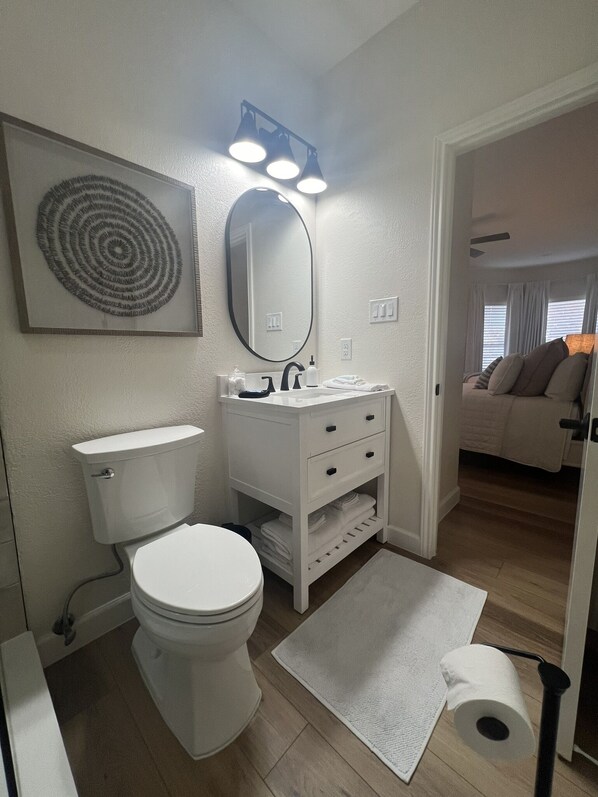 A modern bathroom with a toilet, sink, and mirror. There is a white rug on the floor and a towel rack.