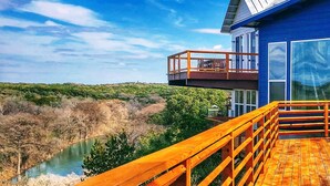 A modern house with a wooden deck overlooking a river and greenery.