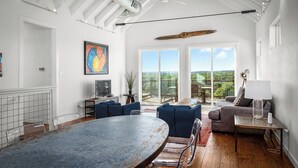A spacious living area with a large table, blue sofas, and a view of the outdoors.