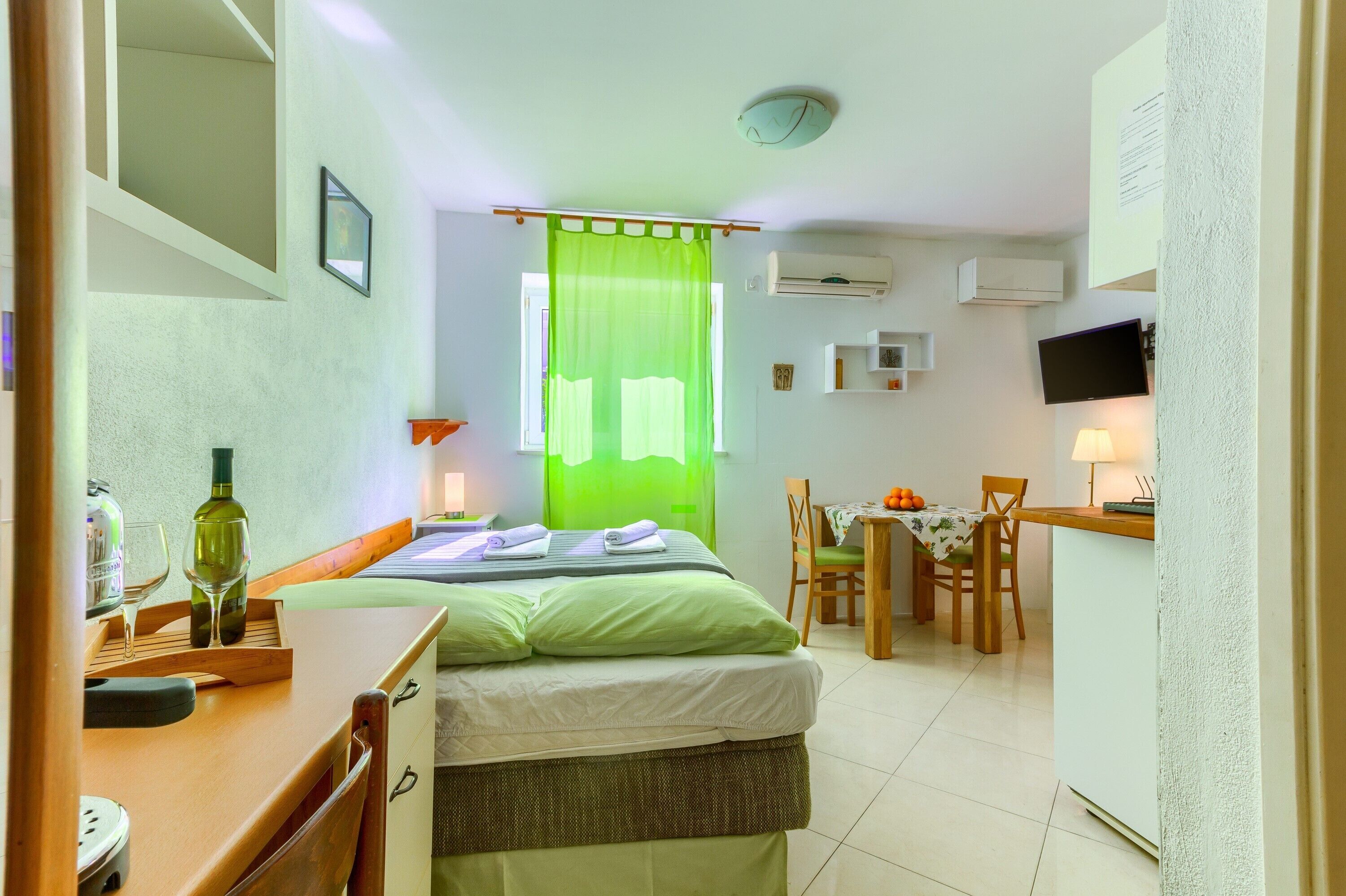 Ett kompakt hotellrum med en säng, ett skrivbord, en stol, en tv och en luftkonditioneringsanläggning.