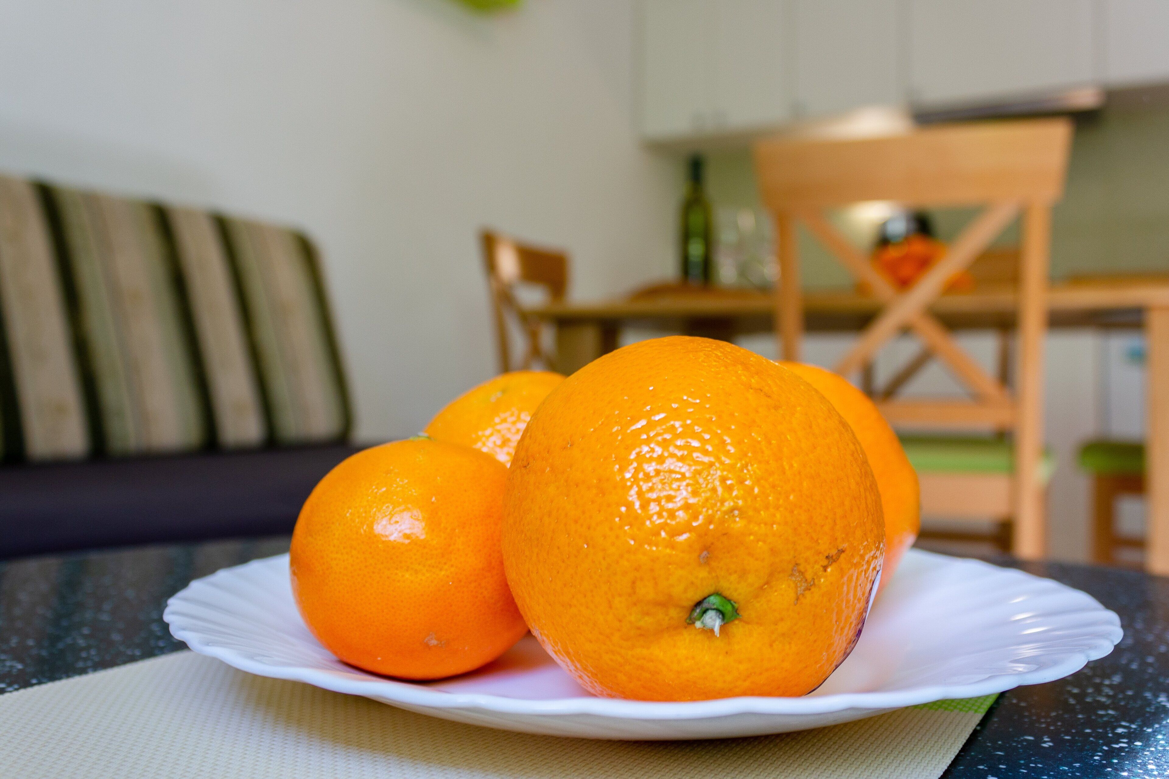 A plate with oranges on a table, a chair, and a couch in the background.