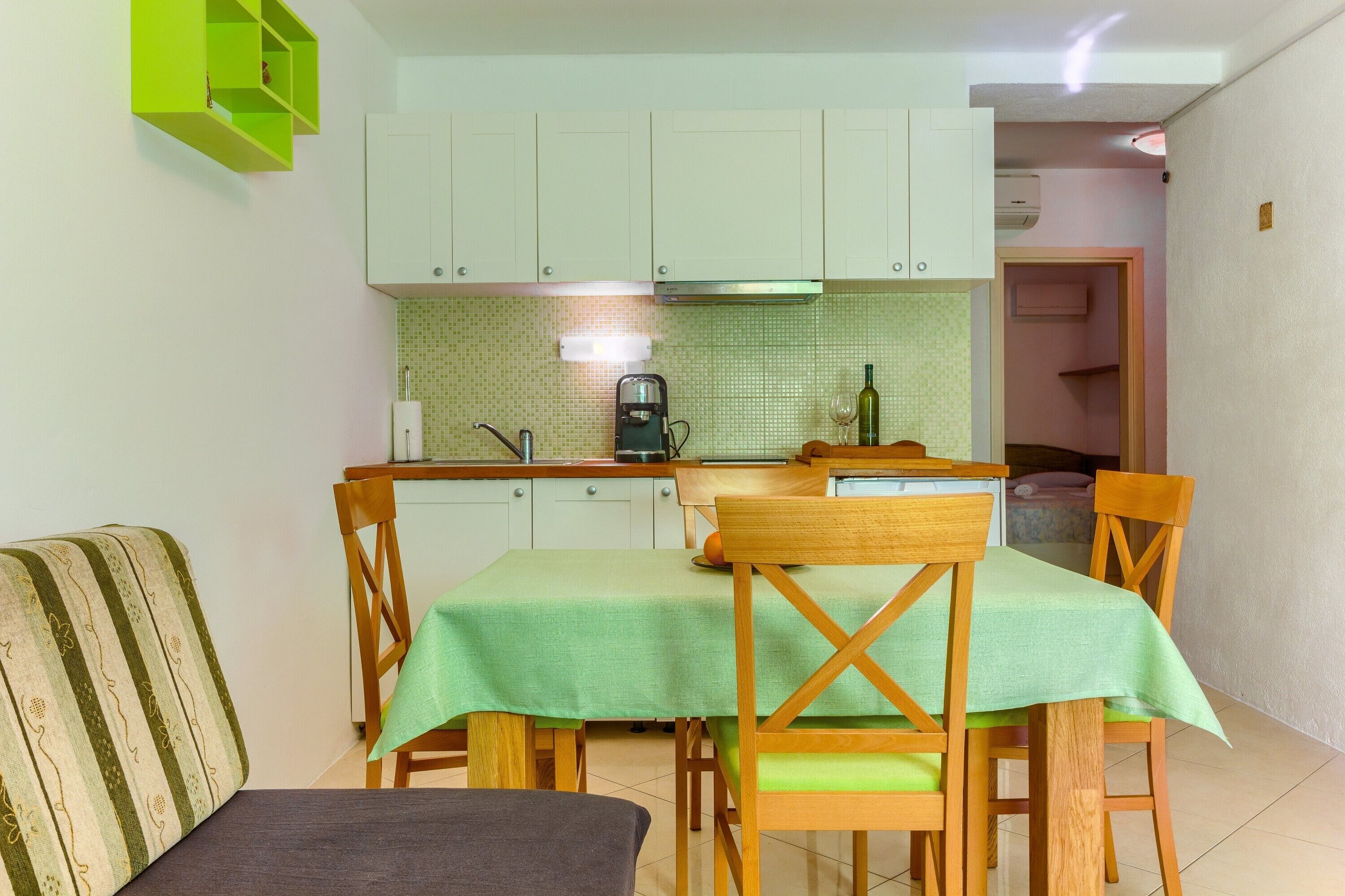 A compact kitchen with white cabinets, a green tiled backsplash, and a dining area with a table set for four.