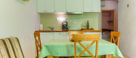A compact kitchen with white cabinets, a green tiled backsplash, and a dining area with a table set for four.