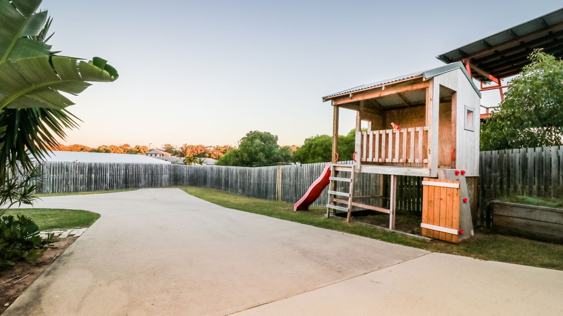 A backyard with a wooden playhouse, a concrete patio, and a wooden fence.