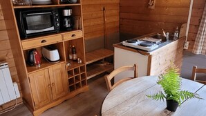 A compact kitchen with a microwave, coffee maker, and a sink. There's a dining table with chairs and a potted plant. - Gite and unusual accommodation (MITZACH)