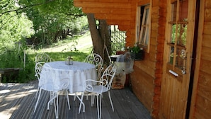 A wooden cabin with a deck, a round table with chairs, and a door with windows. - Gite and unusual accommodation (MITZACH)