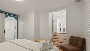 Un dormitorio con una cama, una silla marrón y una escalera que lleva a otra habitación.