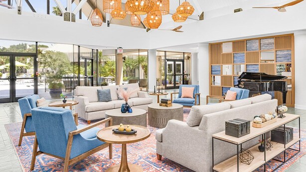 A spacious lobby with a piano, sofas, and a large window offering a view of the outdoors. - Peaceful 2BR Villa at Marriott Sabal Palms – Full Kitchen + Quiet Resort Setting (Orlando)