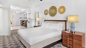 A hotel room with a large bed, a wooden nightstand, two wall-mounted lamps, and a bathroom visible through an open door. - Peaceful 2BR Villa at Marriott Sabal Palms – Full Kitchen + Quiet Resort Setting (Orlando)