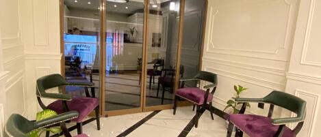 A hotel lobby with a marble floor, a glass door entrance, and two green chairs with purple cushions.