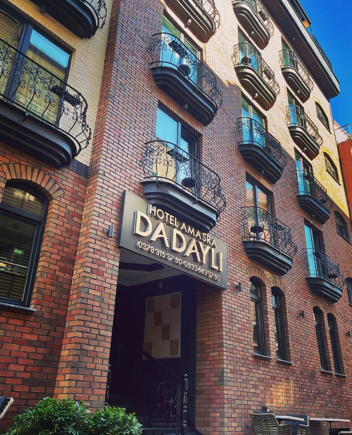 En hotelindgang med et skilt, der viser "HOTEL AMASDA HOTEL DADAYLI" og kontaktoplysninger.