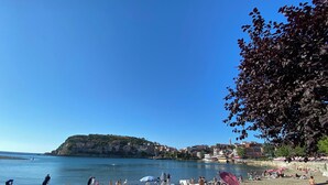 Une plage avec des transats et des parasols, un ciel bleu dégagé et une colline en arrière-plan.