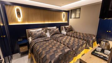 A modern hotel room with two beds, a bedside table, a nightstand, and a wooden side table with a tray of tea and cups.