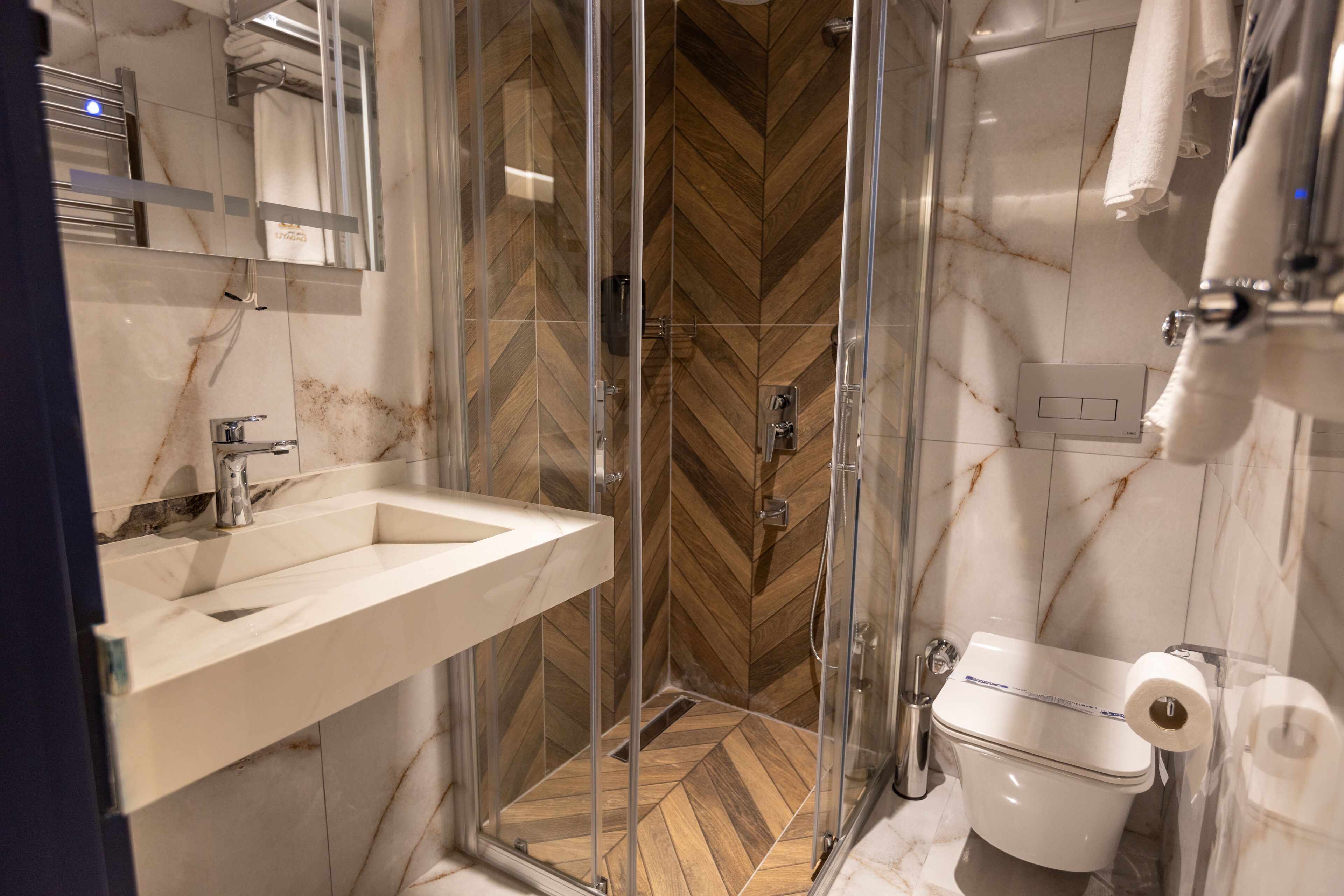 Un baño moderno con ducha envuelta en vidrio, lavamanos de mármol y retrete.