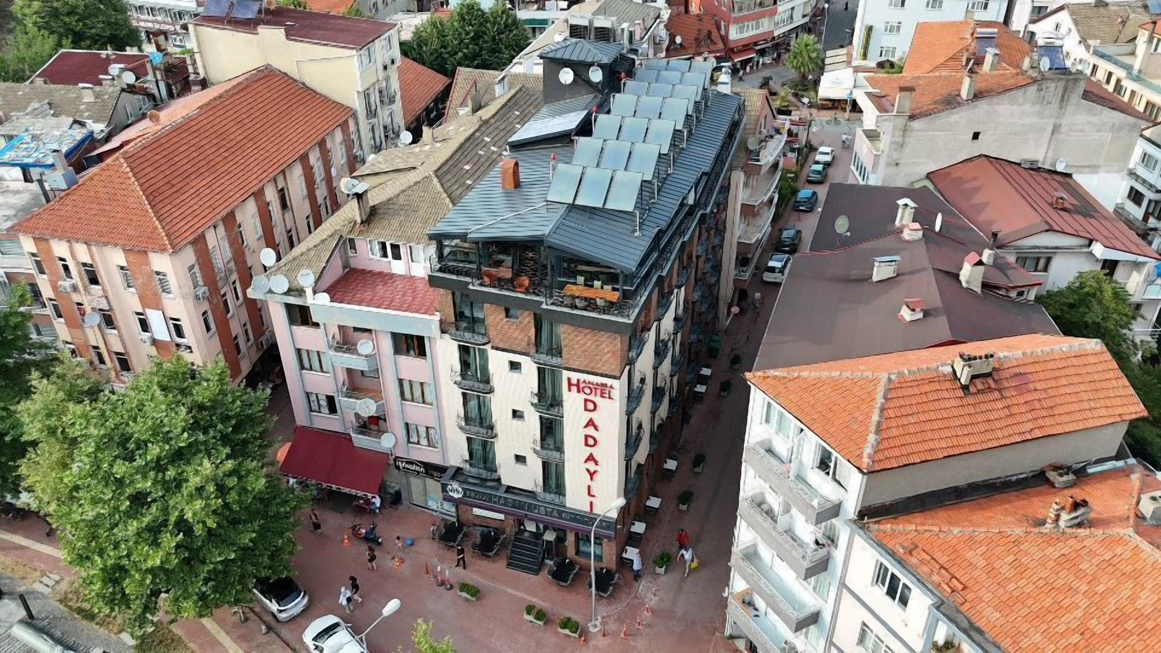 Een meerhoog gebouw met een terras op het dak, een zichtbaar bord met 'Yamama Hotel Dada Yali' en omliggende stadsgebouwen.