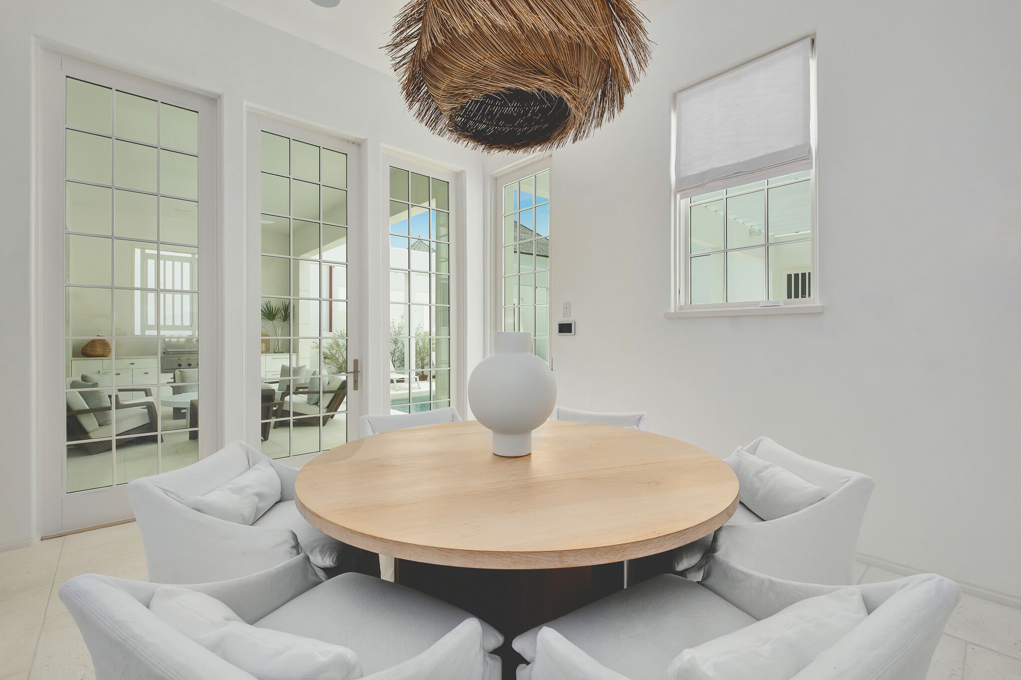 A modern dining area with a round wooden table, white cushioned chairs, and a unique spherical light fixture.