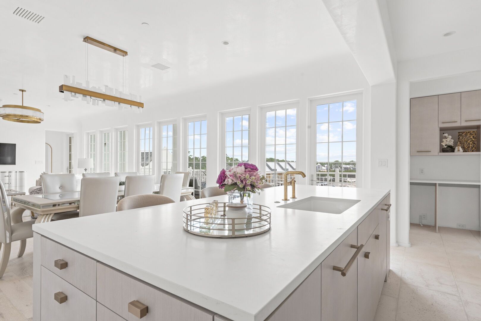 A spacious kitchen with a large island, white cabinetry, and a view of the outdoors.
