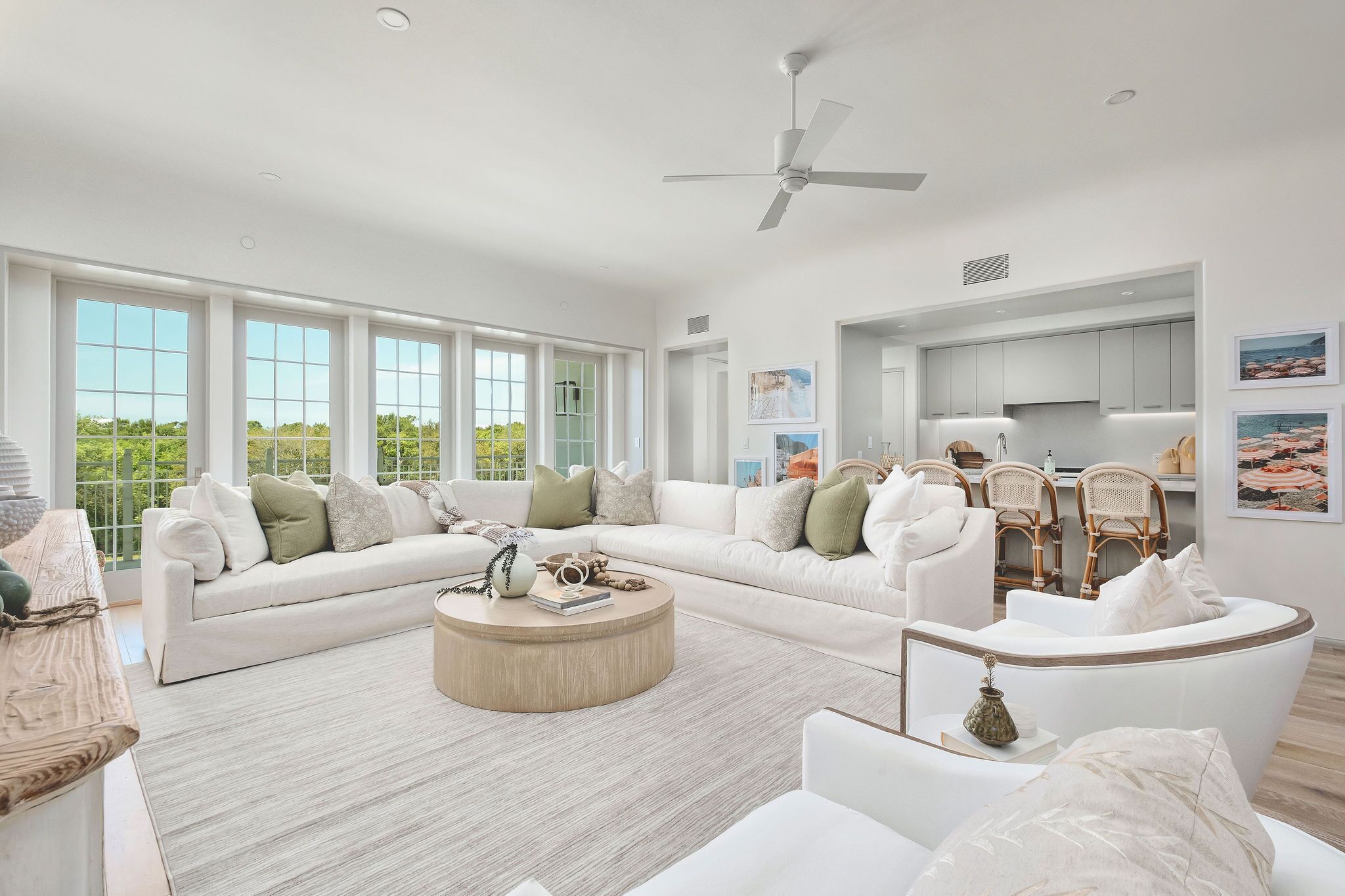 A spacious living room with a white sofa set, a round coffee table, and a dining area with wicker chairs.