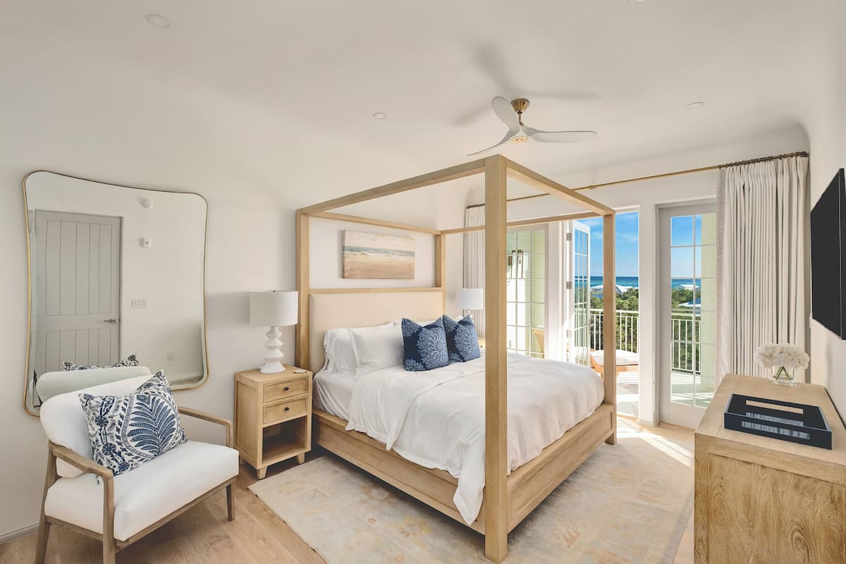 Un dormitorio con cama con dosel, una silla, una mesita de noche y un espejo, con vistas al exterior.
