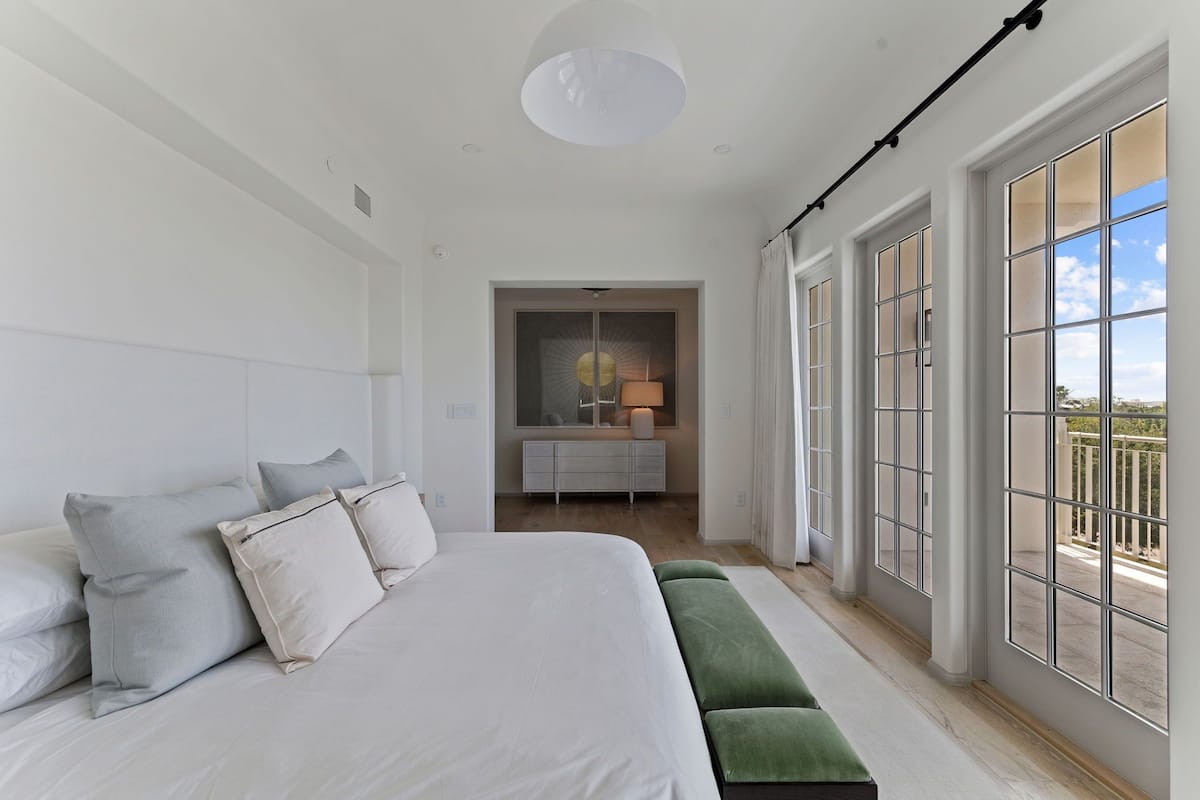 Un dormitorio con una cama grande, un banco, un aparador y vistas al exterior.