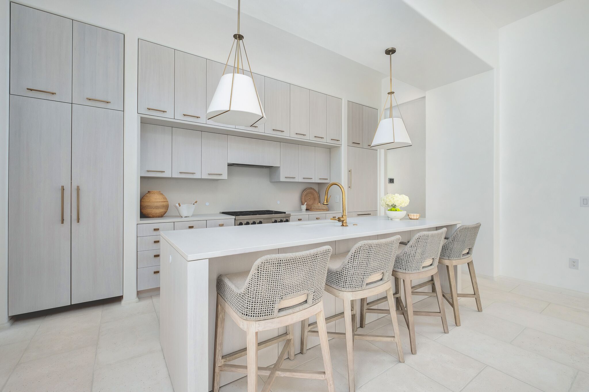 A modern kitchen with light grey cabinets, a white island with bar stools, and pendant lighting.