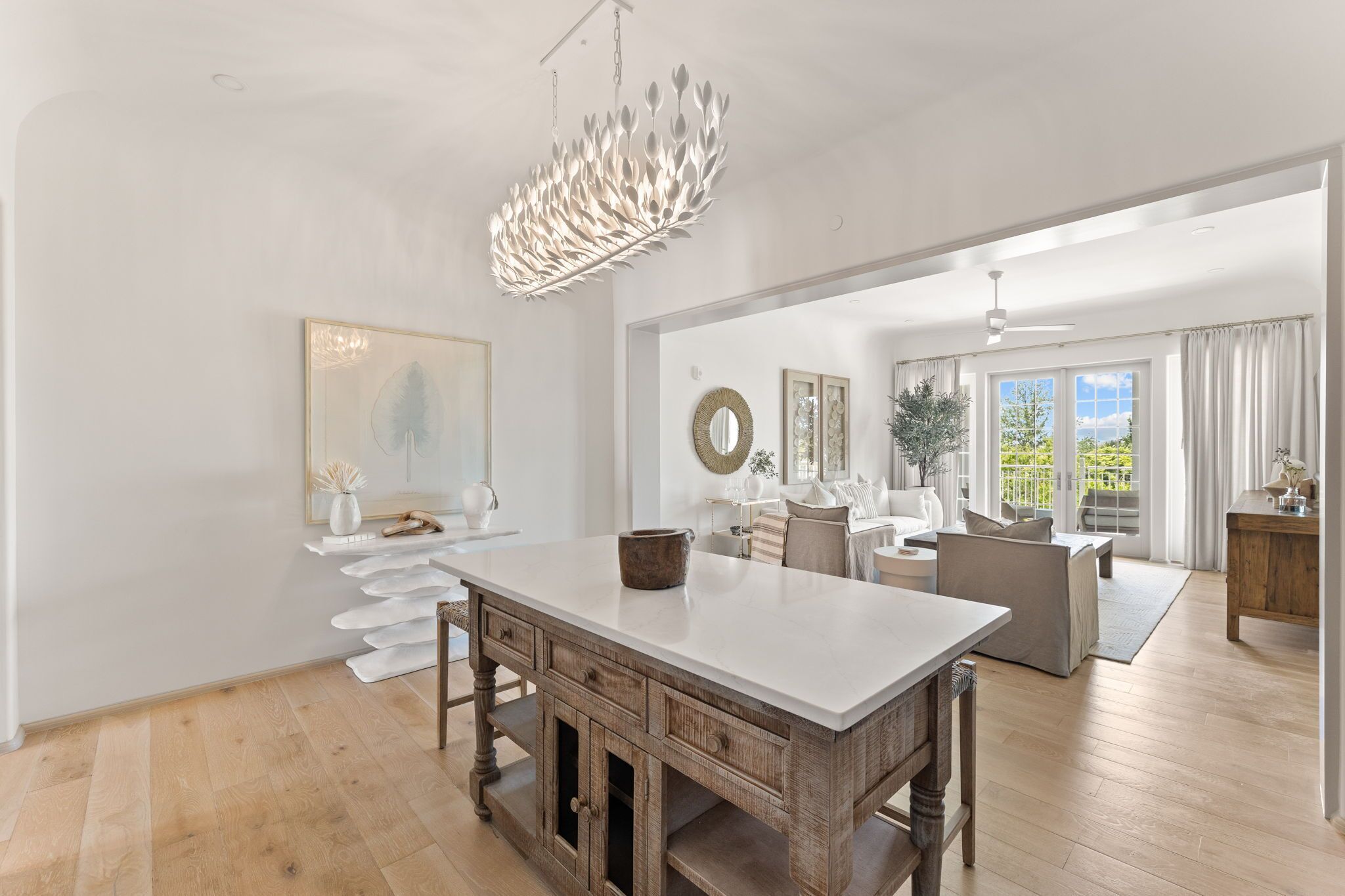 A spacious kitchen with a large island, modern pendant light, and a view to a balcony.