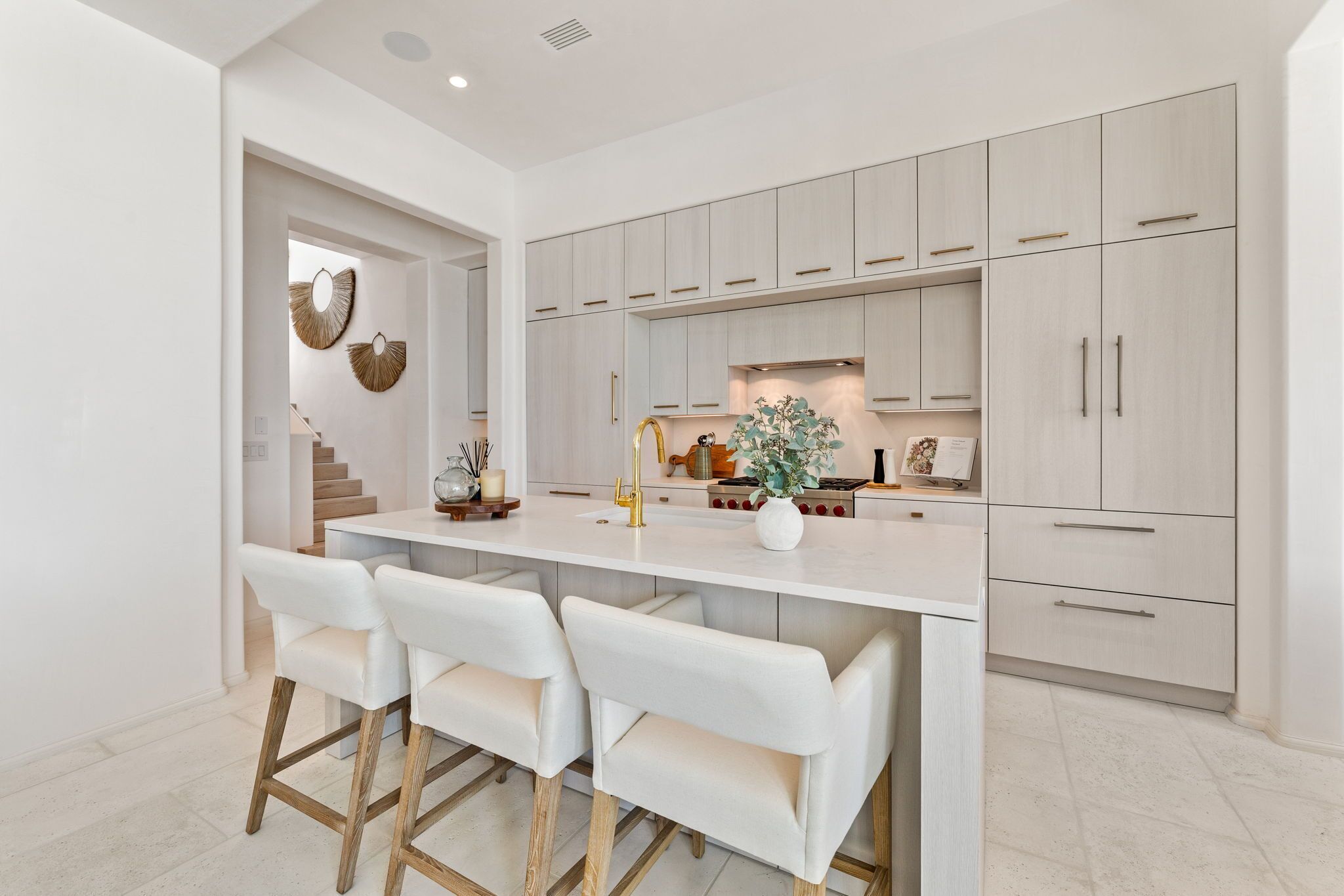 A modern kitchen with white cabinetry, a central island with bar stools, and a staircase leading to another level.