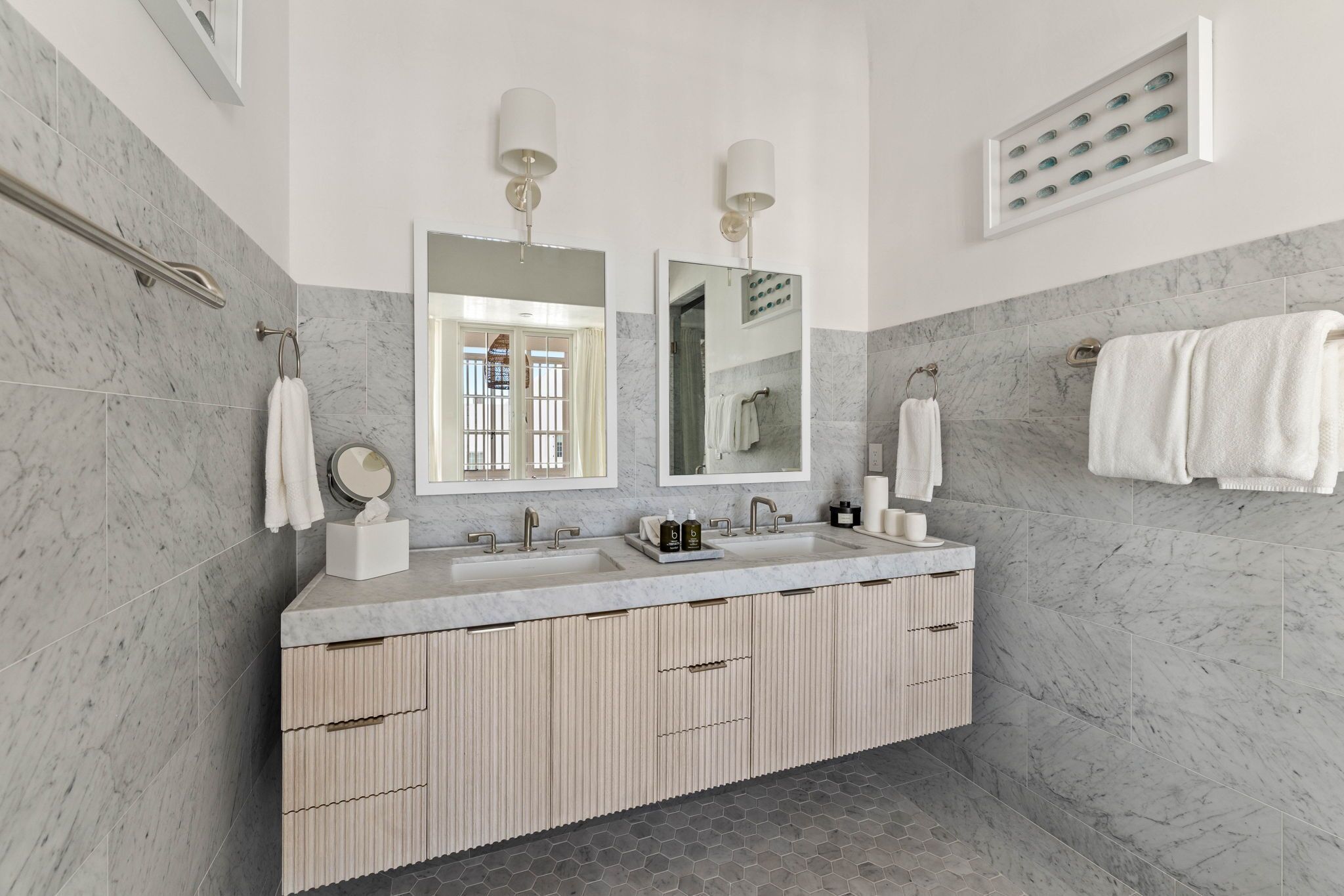 A modern bathroom with a marble sink, two mirrors, and a vanity with storage.