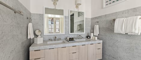 A modern bathroom with a marble sink, two mirrors, and a vanity with storage.