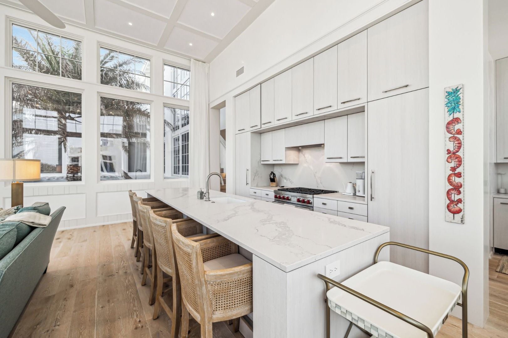 A modern kitchen with a large island, white cabinetry, and a view of palm trees outside.